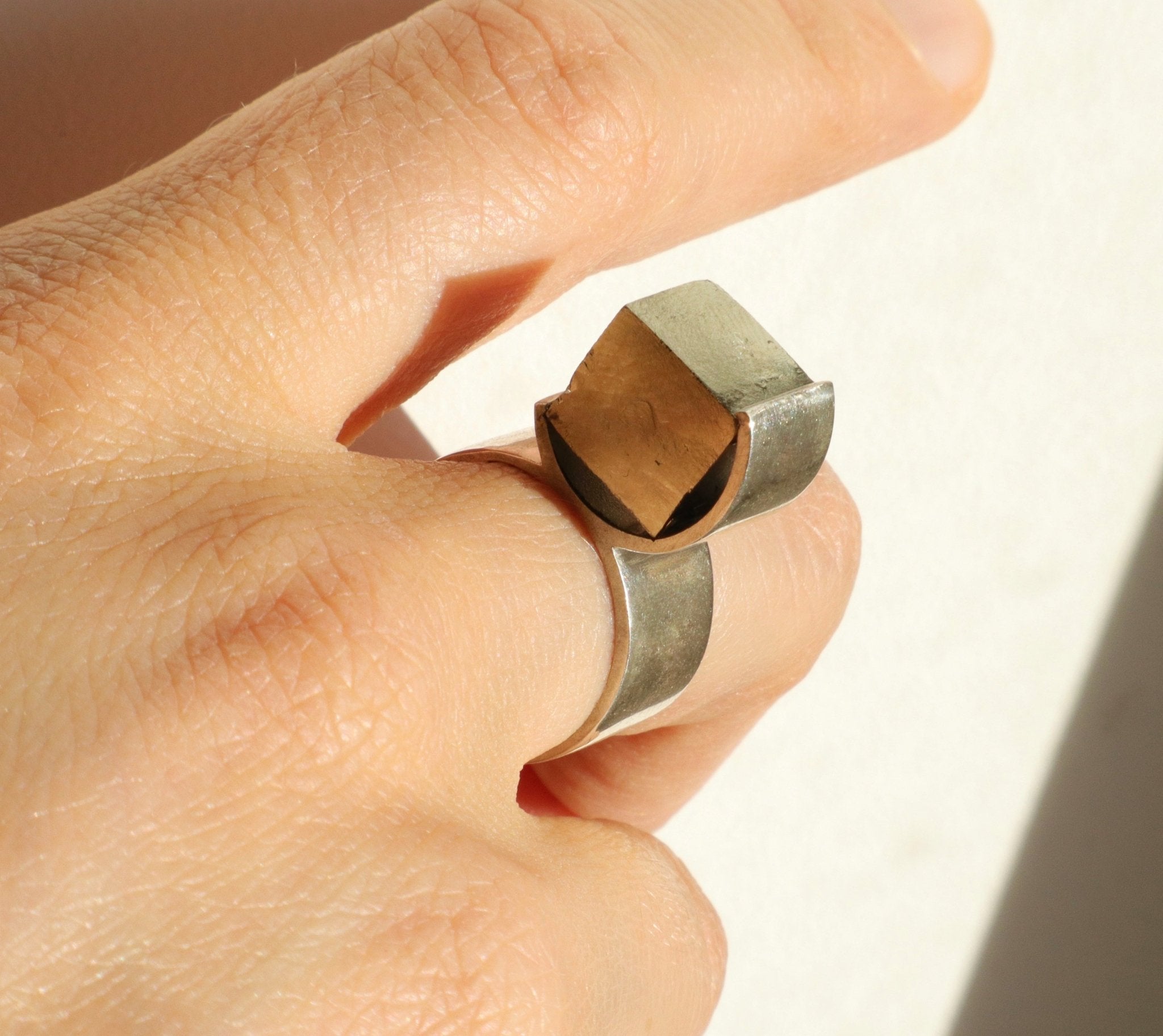 Gros plan de la bague O en argent portée sur la main, détail du serti circulaire et de la pyrite brute naturelle, Atelier Grandval.